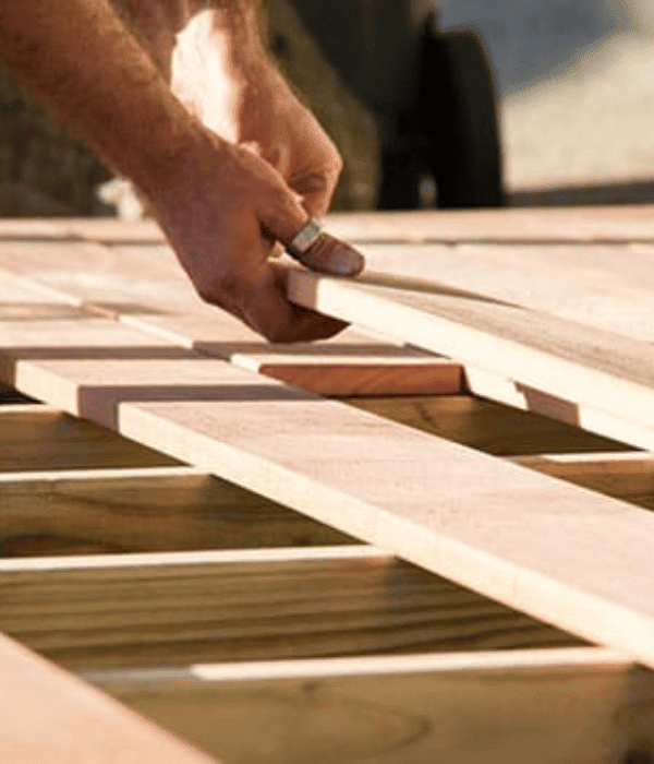 A person measuring and aligning wooden planks on a wooden frame, using a tape measure in natural light.